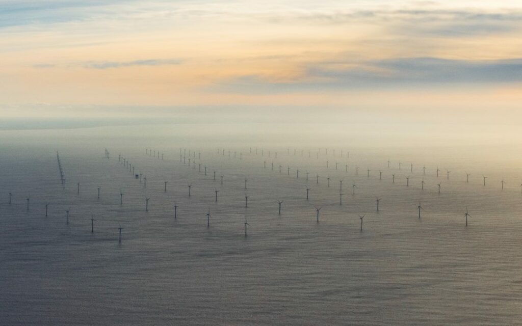 Bird's perspective photo of a large offshore windfarm. Multiple turbines with access gates standing in the sea